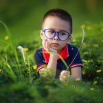 child in grassy field wearing big glasses